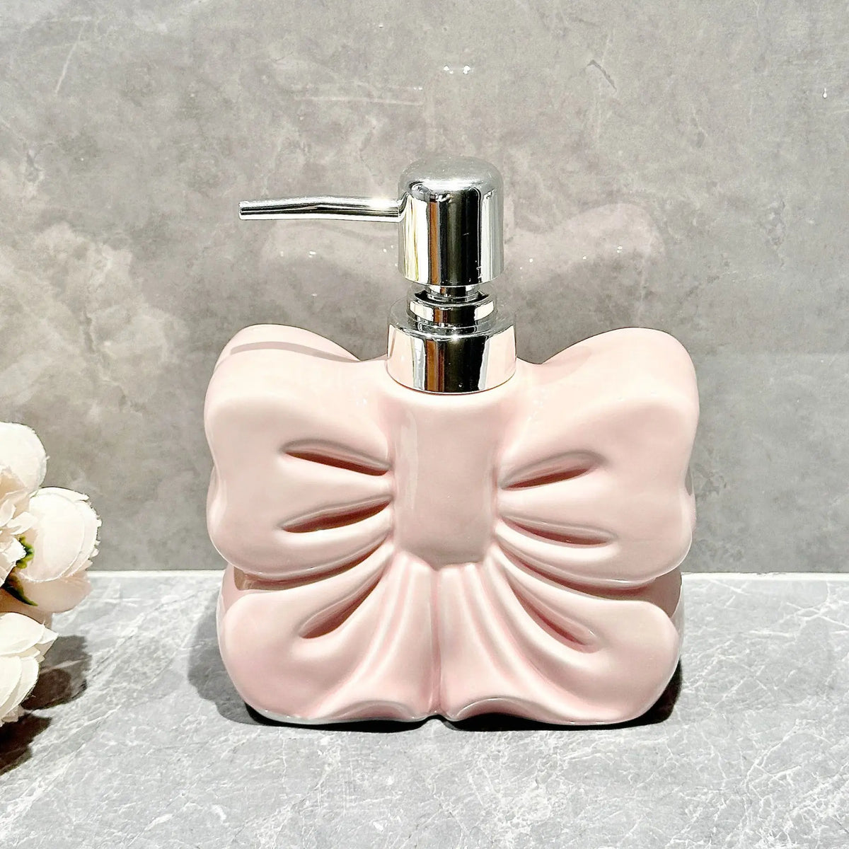 A pink ceramic pump dispenser with a silver pump mechanism sitting on a gray surface.