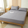A gray waterproof fitted mattress protector is displayed on a wooden bed frame with a quilted cover.