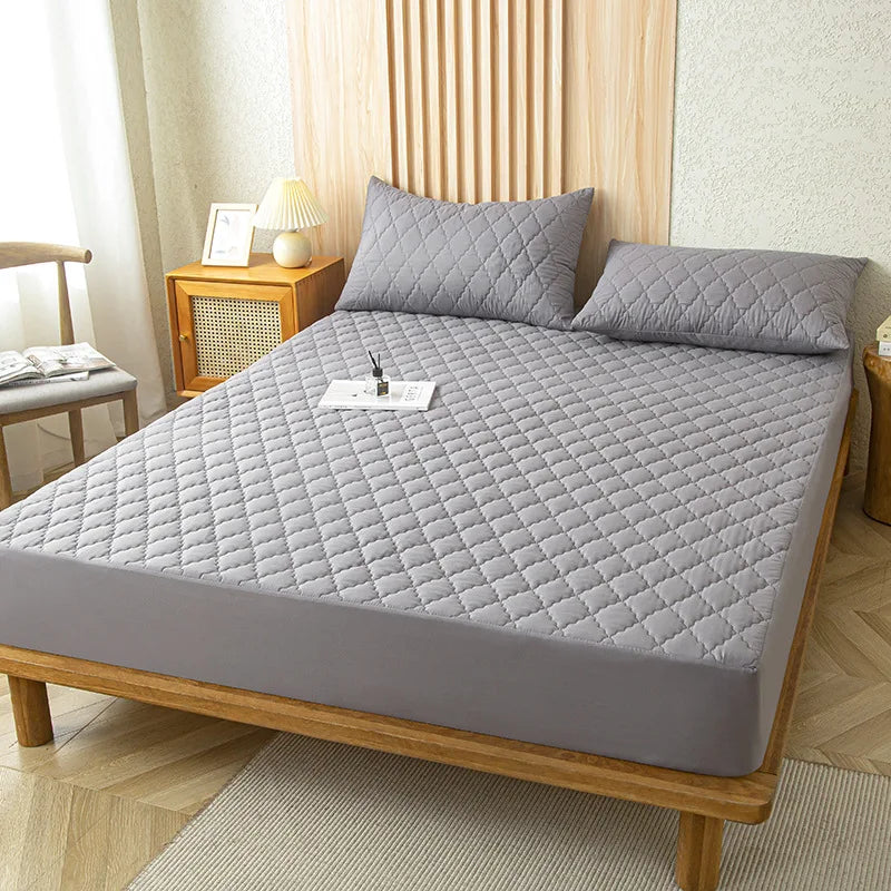 A gray waterproof fitted mattress protector is displayed on a wooden bed frame with a quilted cover.