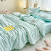 A light mint green breathable summer seersucker quilt spread across a bed with white bedding and a small white stuffed animal