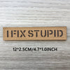 A rectangular brown woven patch with the text IFIXSTUPID printed on it, shown against a light wooden background.