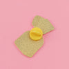 A gold glitter enamel pin shaped like a strawberry is displayed on a pink background.