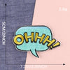 A teal embroidered lettering patch shaped like an exclamation mark on a gray fabric background.