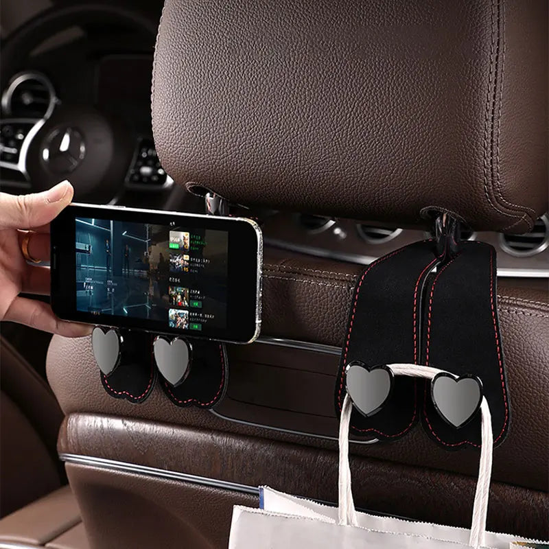 A black car seat headrest hook with dual fabric loops is shown attached to a leather seat, ready for hanging bags or phones.