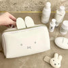 A white Miffy cartoon rabbit cosmetic storage bag is shown next to various Lancôme products on a marble surface.