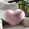 A fluffy pink heart-shaped throw pillow resting on a light-colored sofa.