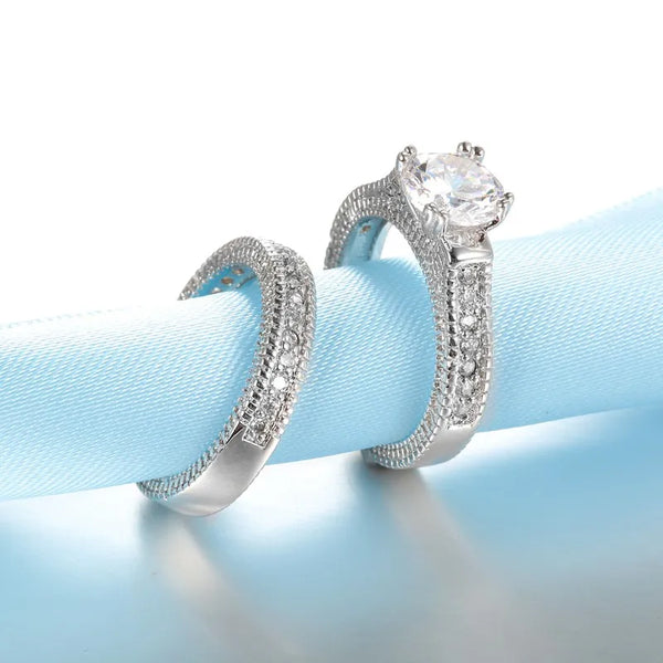Un par de anillos de compromiso de plata de ley 925 con engastes de diamantes, exhibidos en una cinta azul claro.