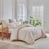 A beige duvet cover set with a subtle leaf print pattern displayed on a bed in a bright, minimalist room.