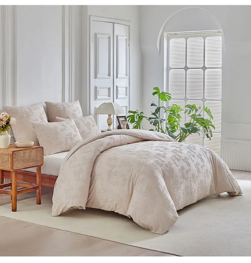A beige duvet cover set with a subtle leaf print pattern displayed on a bed in a bright, minimalist room.