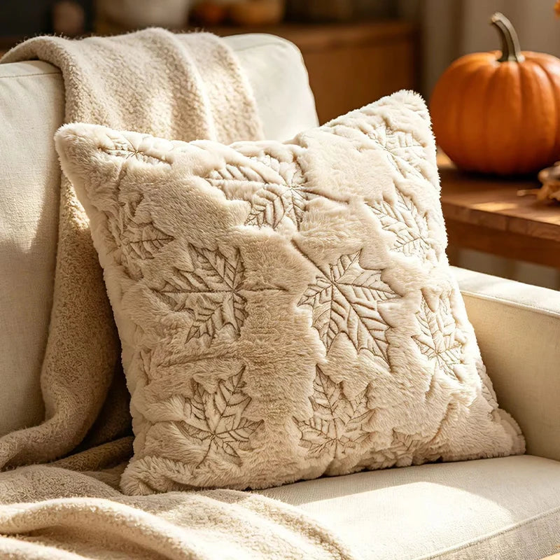 A cream-colored plush throw pillow with embossed maple leaf patterns resting on a light sofa.