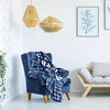 A deep blue fleece throw blanket draped over a velvet armchair in a bright room.