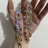 A hand holds a long, iridescent resin chain replacement strap with gold-toned clasps.