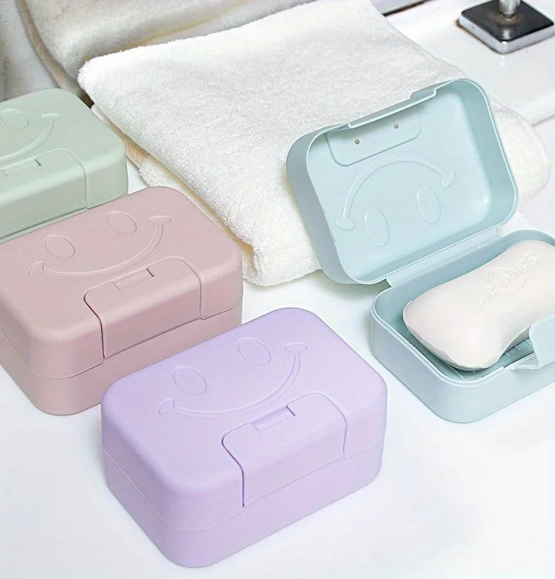 A collection of pastel colored smiley face lidded soap dishes and a white towel are displayed on a white surface.