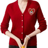 A woman models a red knitted sweater with a heart-shaped rhinestone patch on the chest.