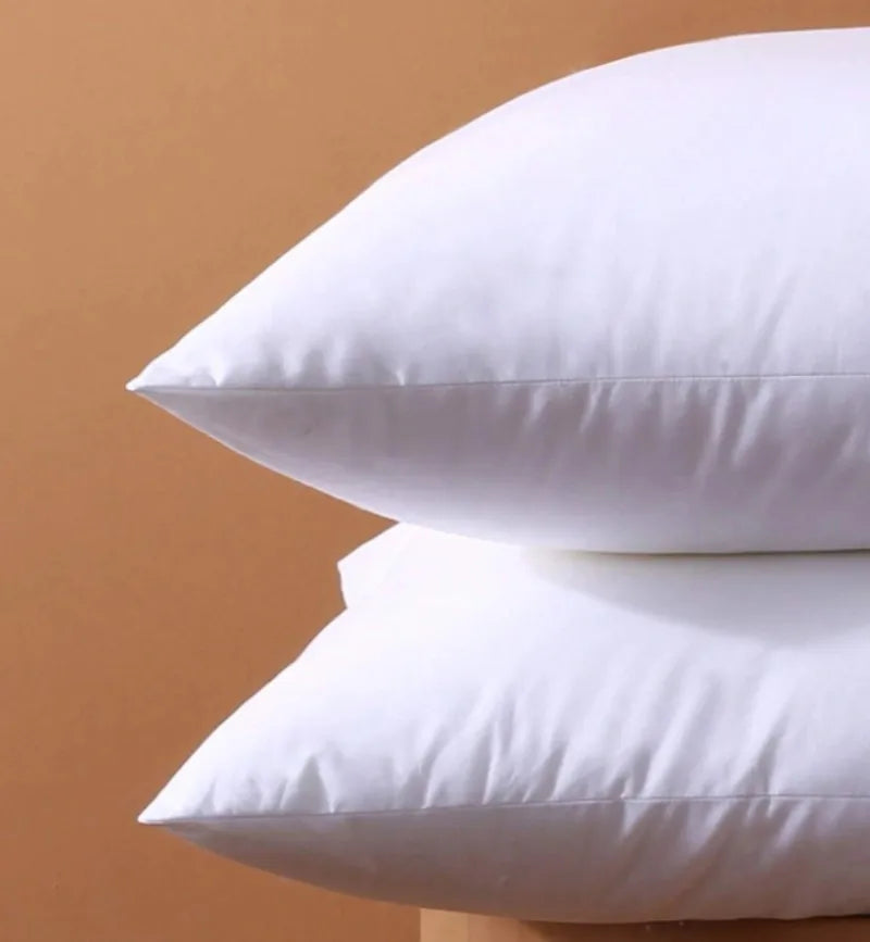 A stack of white square cushions with a smooth, rounded shape against a beige background.