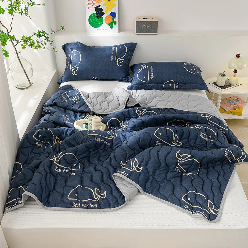 A navy blue quilted blanket with a repeating fish pattern is displayed on a bed, alongside matching pillows.