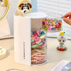 Clear acrylic hair accessories organizer with rotating compartments holding colorful hair ties and a yellow stuffed animal.