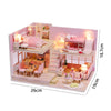 A miniature wooden dollhouse building kit featuring pink furniture and interior rooms with lighting.