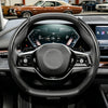 Close-up view of a black steering wheel with carbon fiber pattern grips and controls inside a vehicle