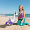 A young girl is posing with a mermaid bikini costume and a lawn goose statue on a sandy beach.