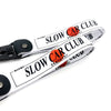 A white nylon keychain with black steel clip featuring the text SLOW CAR CLUB in orange and black.