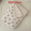 A light pink floral muslin baby blanket with a beige lining is shown folded on a light fabric background.