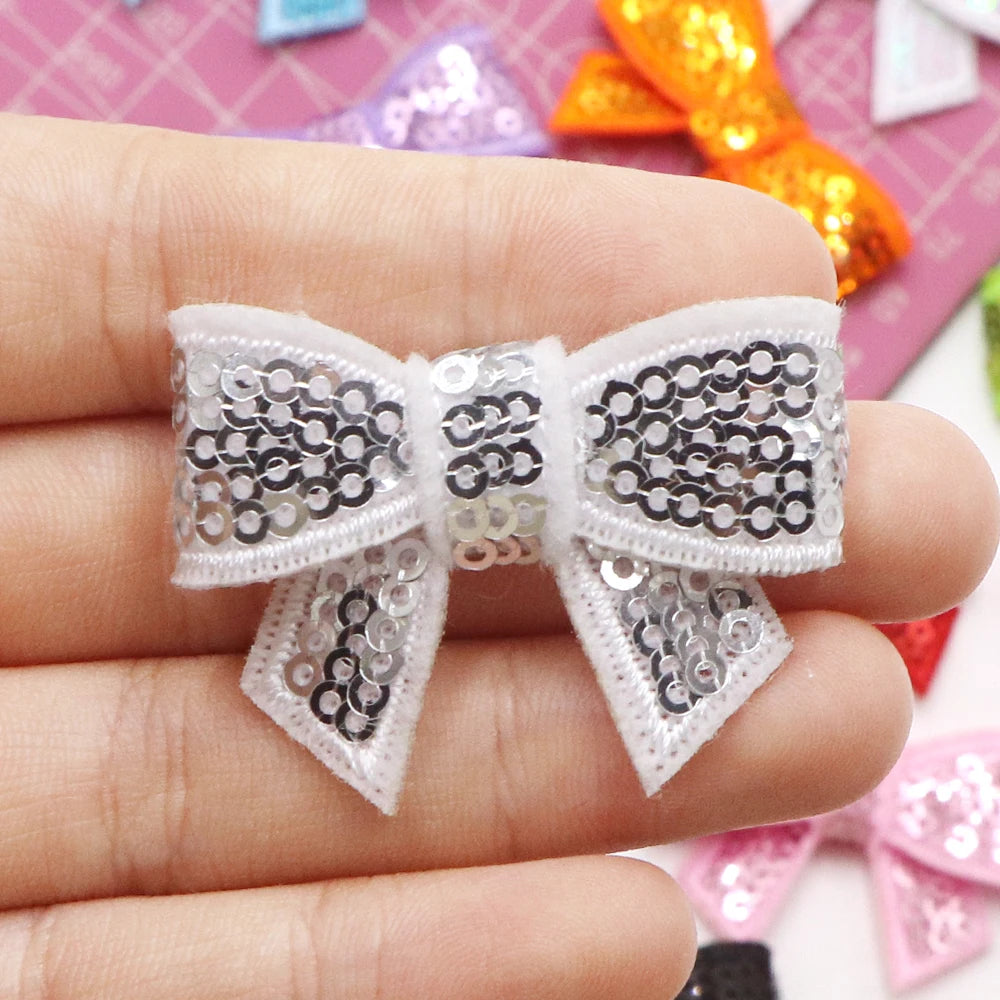A hand holds a white sequin bow patch for DIY crafts, featuring black and silver sequins.