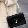 A black leather purse with a gold chain and pearl accents is shown against a white fur background.