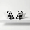 A pair of cute black and white panda figurines sitting on a white surface.