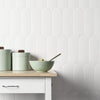 A light green bowl and matching storage containers are displayed on a white wooden surface against a white textured wall.