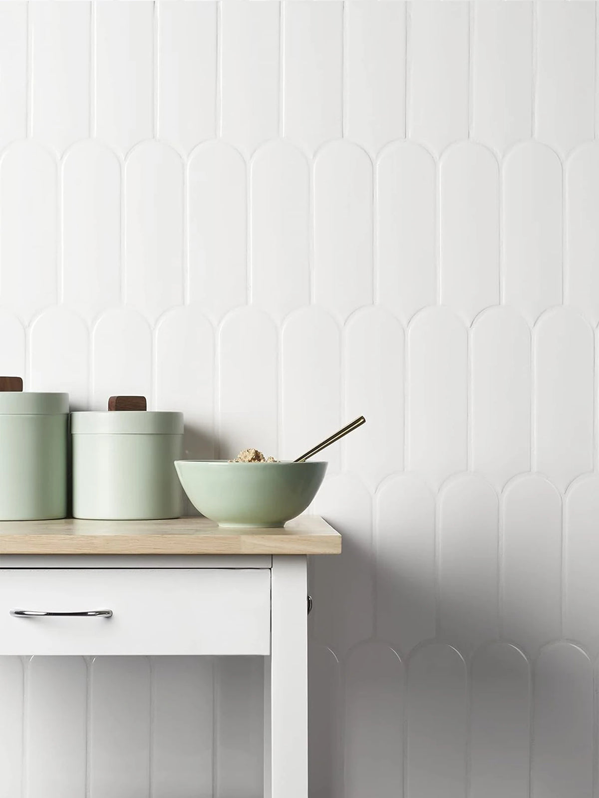 A light green bowl and matching storage containers are displayed on a white wooden surface against a white textured wall.