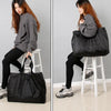 A woman is shown holding a black reusable large-capacity grocery tote with a zipper on a white stool.