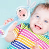 A baby is holding a light blue musical rabbit rattle and teether toy.
