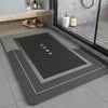 A rectangular gray bath mat with a black area marked HOME and a silver border, placed on a tiled floor.