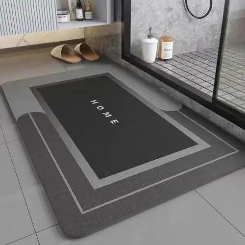 A rectangular gray bath mat with a black area marked HOME and a silver border, placed on a tiled floor.