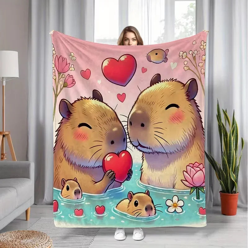 A pink flannel throw blanket featuring a cartoon illustration of two cute capybaras with hearts.
