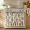 A white farmhouse oven skirt with floral pattern and blue ruffle trim installed on a stove.