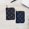 A dark navy patterned compact zippered card holder wallet resting on a light wooden surface next to a pen and a white noteboo