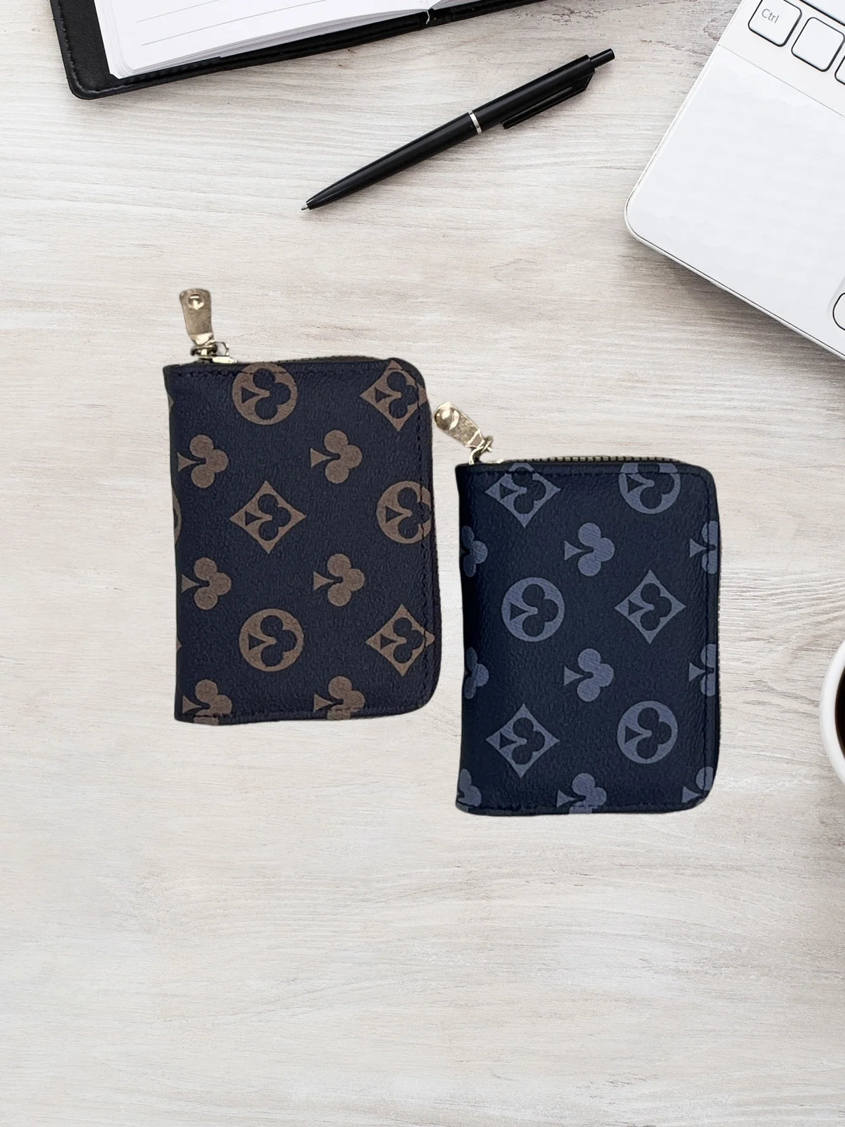 A dark navy patterned compact zippered card holder wallet resting on a light wooden surface next to a pen and a white noteboo