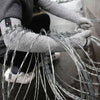 A person wearing protective arm sleeves is handling a bundle of thin, metallic wires.