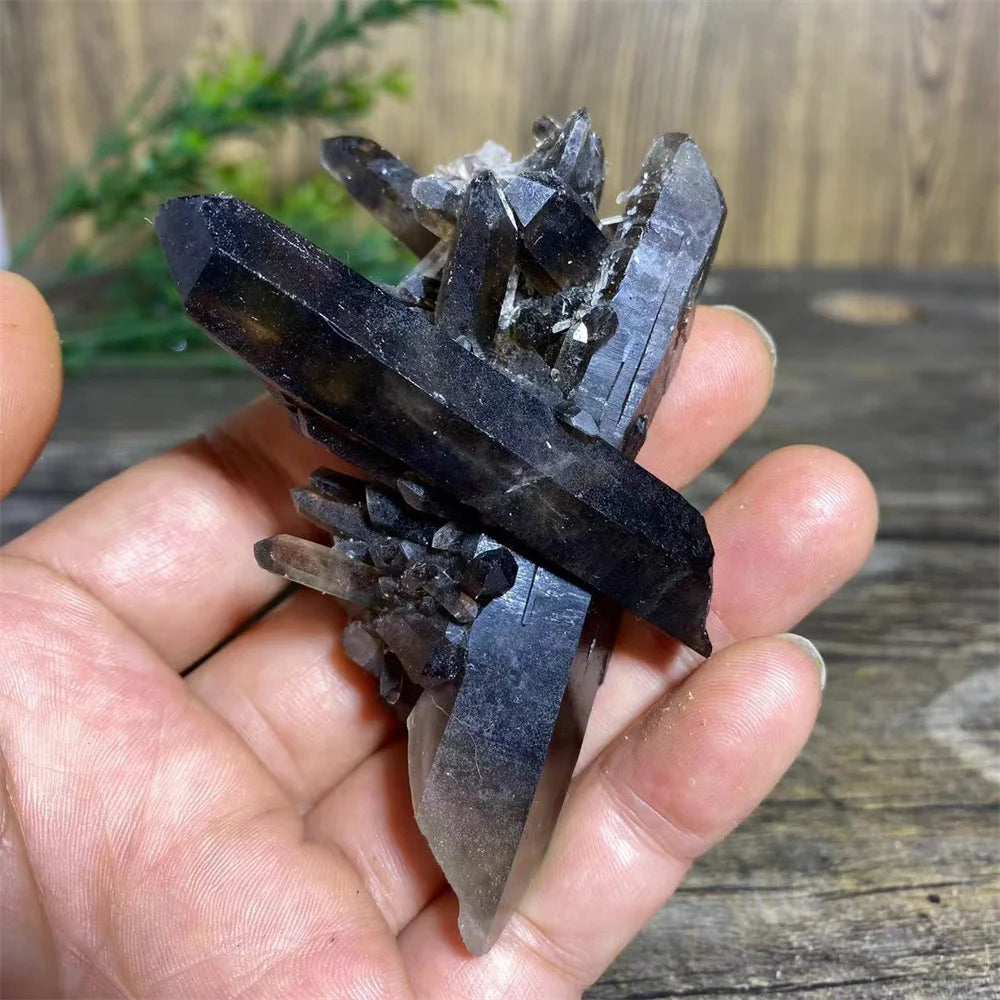 A hand holds a cluster of dark purple and smoky quartz crystals on a wooden surface.
