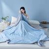 Light blue cooling summer quilt draped on a bed, with a woman resting her head on the fabric.