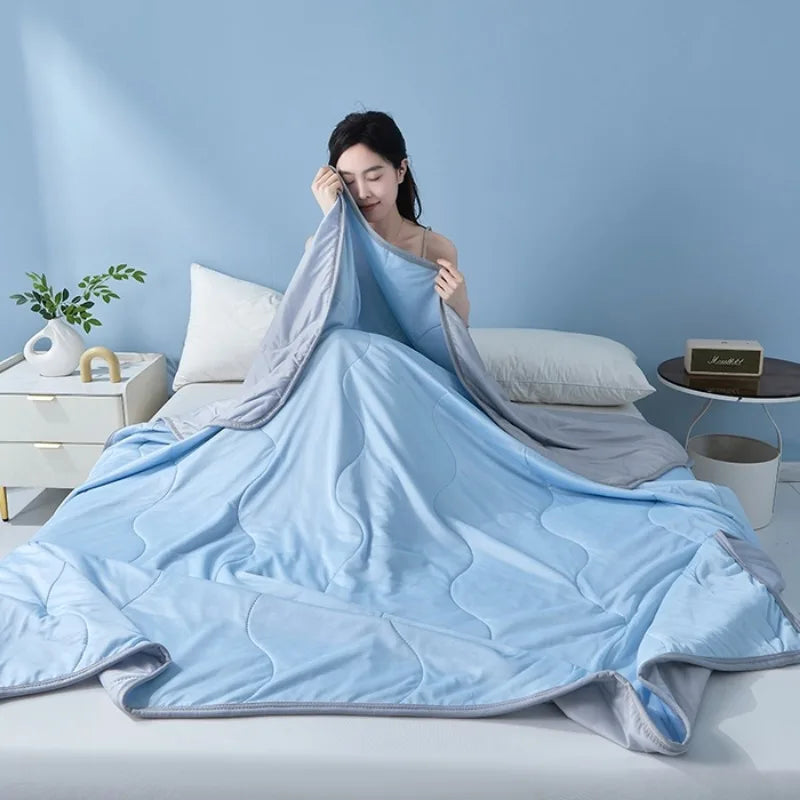 Light blue cooling summer quilt draped on a bed, with a woman resting her head on the fabric.