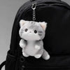 A soft grey cat plush charm hangs from a zipper pull on a black backpack.