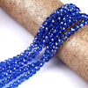 Blue faceted crystal glass spacer beads threaded onto a golden brown paper roll.