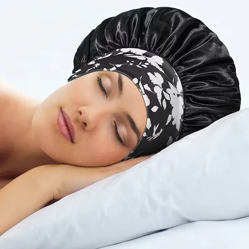 A woman is sleeping wearing a black silk satin sleep bonnet with a white floral elastic band.