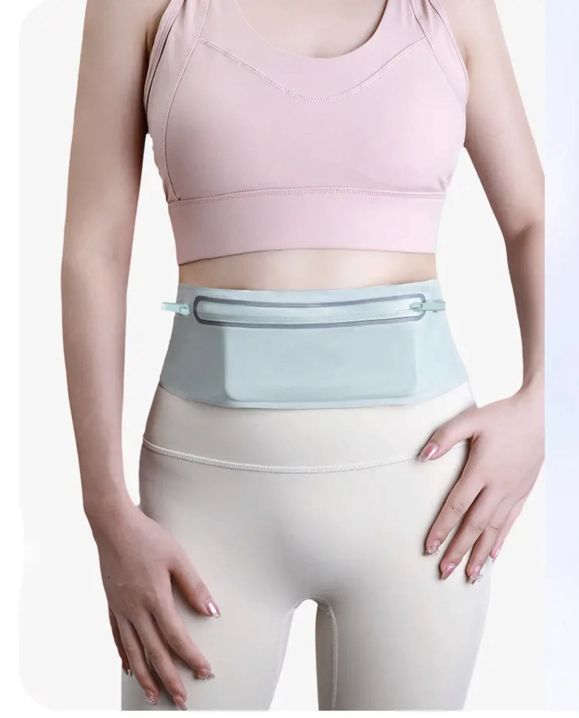 A woman models a light pink sports bra and a light blue running waist pack over beige leggings.