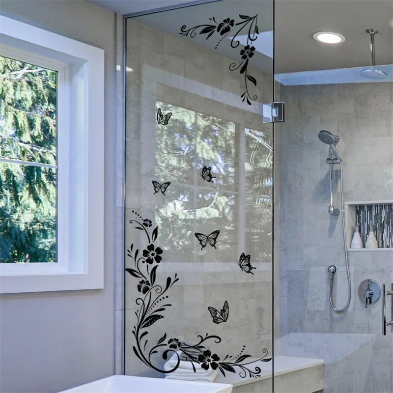 A glass shower enclosure featuring black flower and butterfly decorative vinyl stickers on the door panel.