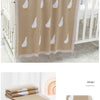 A beige cotton baby swaddle blanket with a white cartoon bird print hanging on a wooden crib railing.