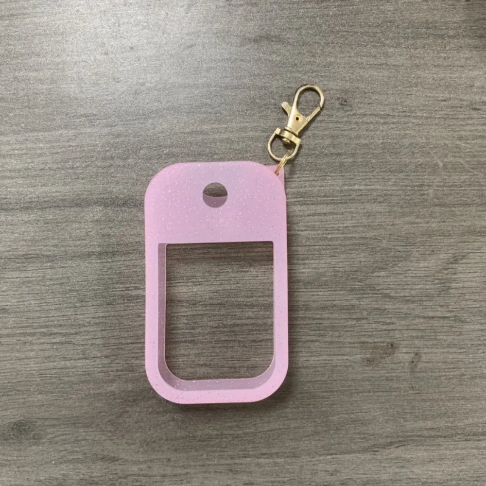 A pink silicone protective case for a hand sanitizer spray attached to a gold keyring.